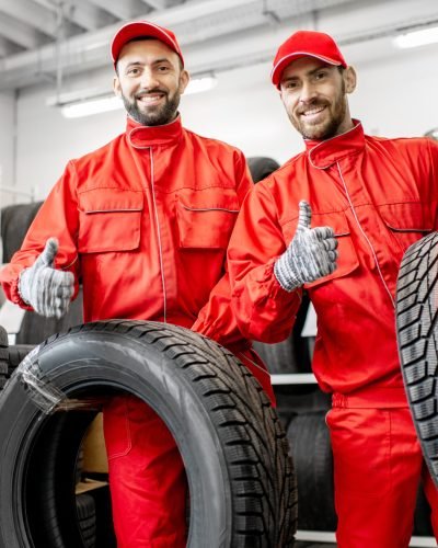 Portrait of a two workers in red uniform with car tires at the warehouse of the car service