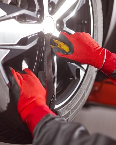 Unrecognizable man in gloves and uniform screwing in wheel while fixing car in garage
